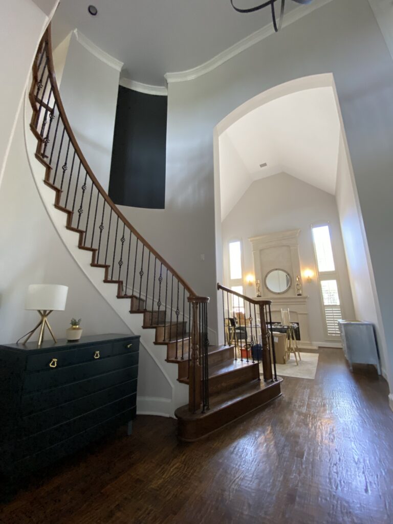 main entry with a curved staircase painted a light neutral blue with cutout portions a dark grey offset by the bright white entryway just beyond